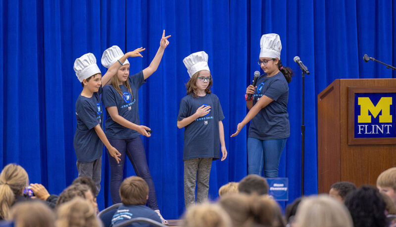 A team of young students in chef's hats presenting their project.