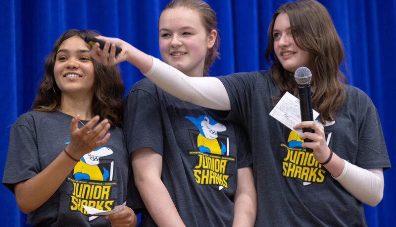 Three young female students on stage presenting their project.