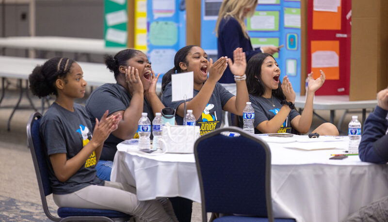 Young student attendees of the Young Sharks competition sitting at a table clapping.