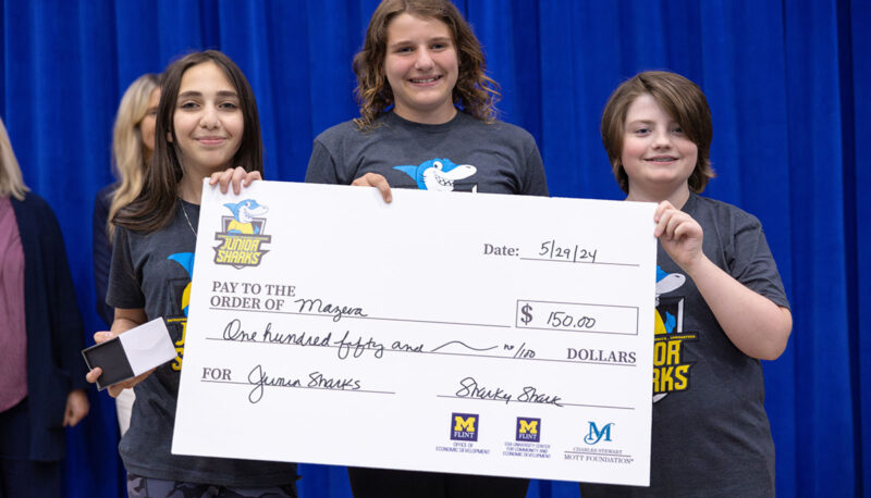 Three female students receiving a big award check on stage