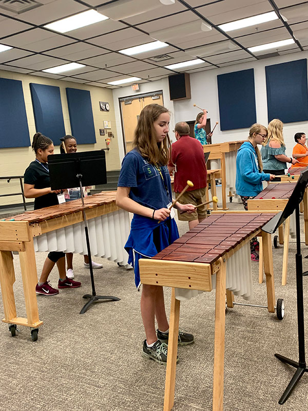 Several teens play marimbas in a classroom.