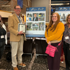 Thomas Henthorn posing with three students with the award in front of a poster detailing their cemetery work.