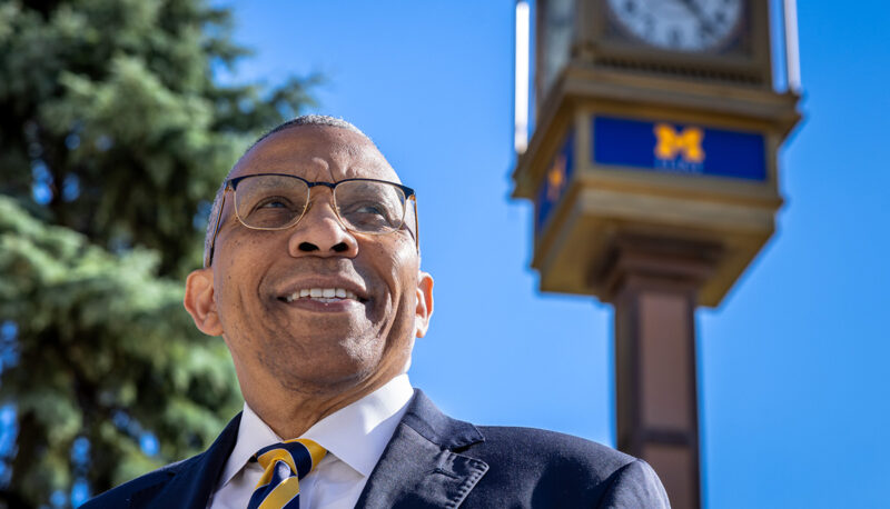 A closeup of Chancellor Alexander with the UM-Flint clock in the background.