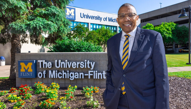 Chancellor Alexander standing next to a UM-Flint sign