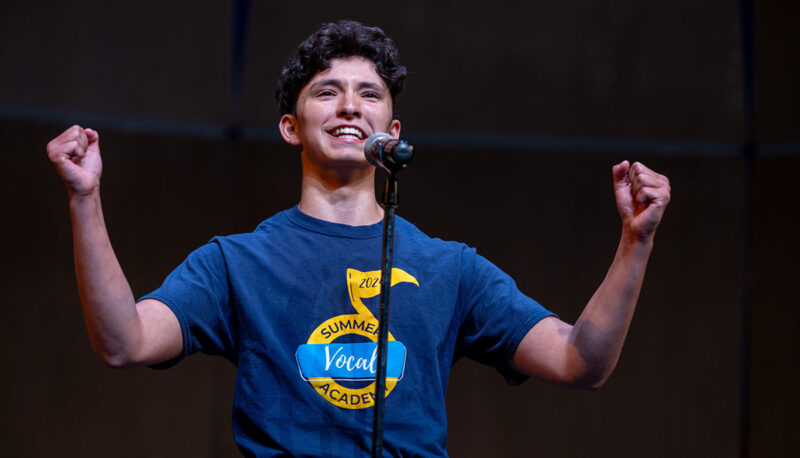 A camper singing into a microphone while raising his fists.