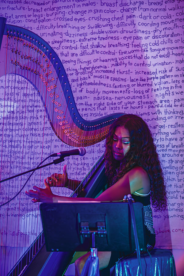 A woman plays a harp with art hanging in the background