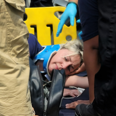 A woman laying on the ground with a neck brace while the crowd gathers around her as part of an accident simulation.