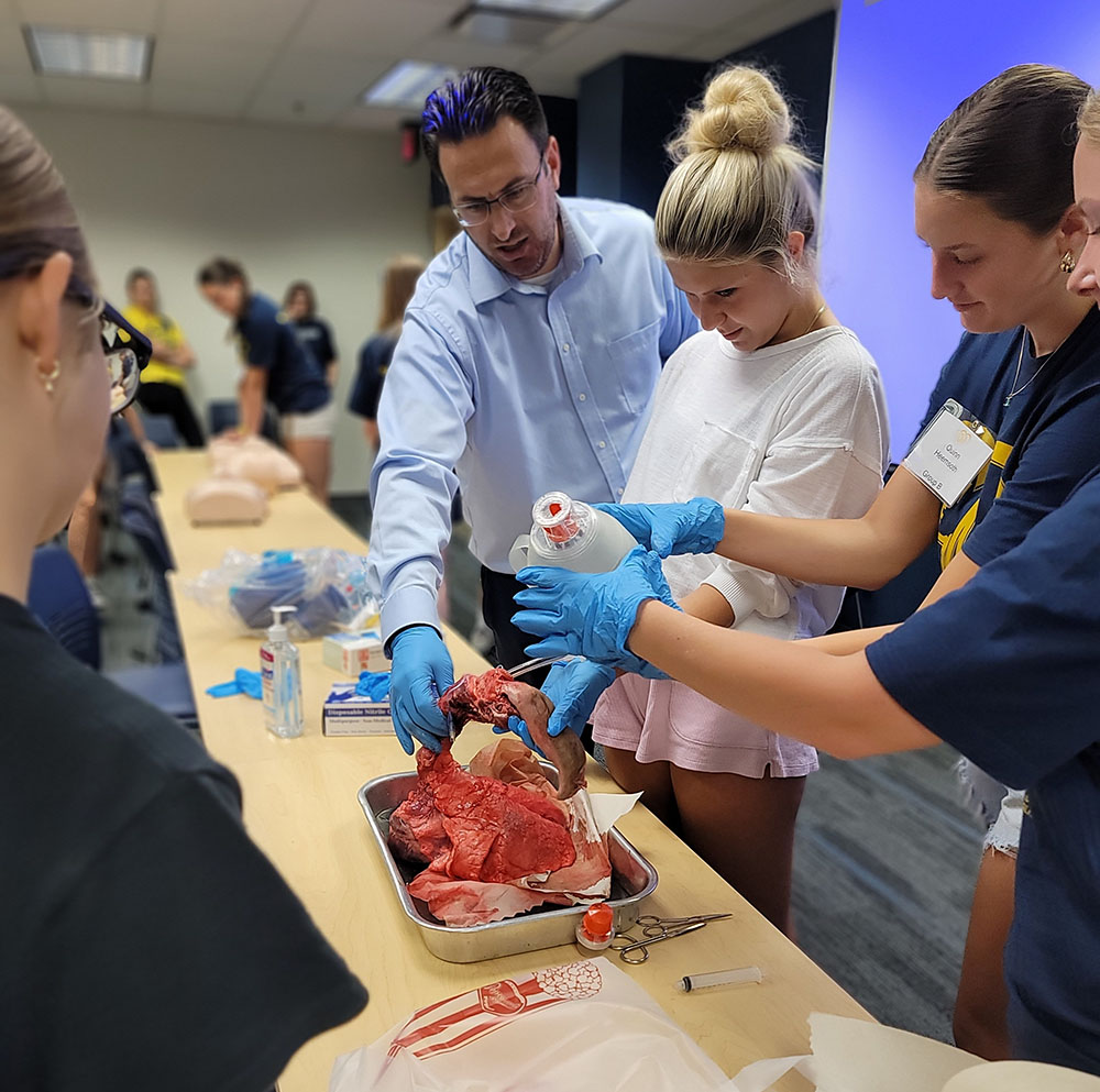 Nicholas Prush, assistant professor and director of public health sciences, works with summer camp students to intubate a set of pig lungs.