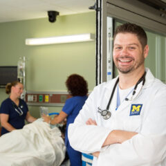 A nursing student in a white coat posing for a photo.