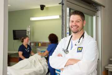 A nursing student in a white coat posing for a photo.