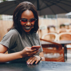 A woman wearing heart sunglasses smiling while looking at her phone