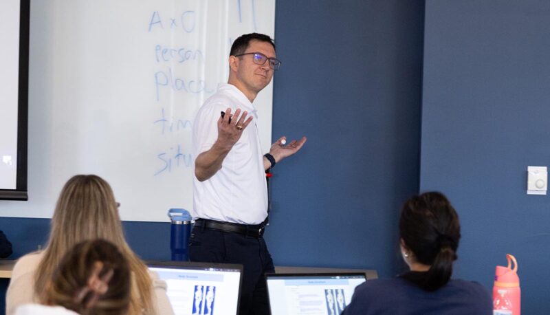 An instructor lecturing at the head of a classroom.