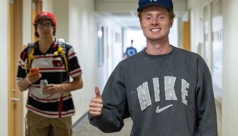 Two students walking in the hallways of the White Building. One is giving a thumbs up