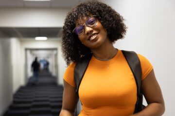 A student in an orange shirt smiling in an MSB hallway.