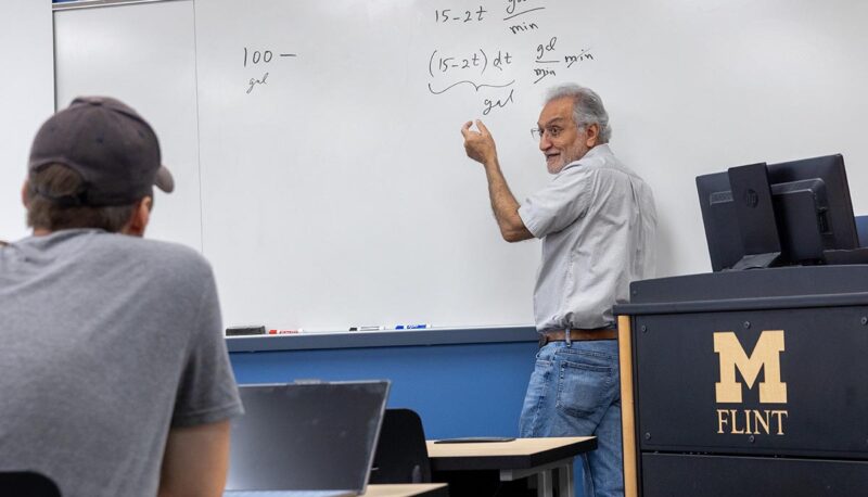 A professor lecturing and writing formulas on a white board.