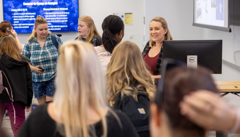 A group of people standing around and talking in a classroom.