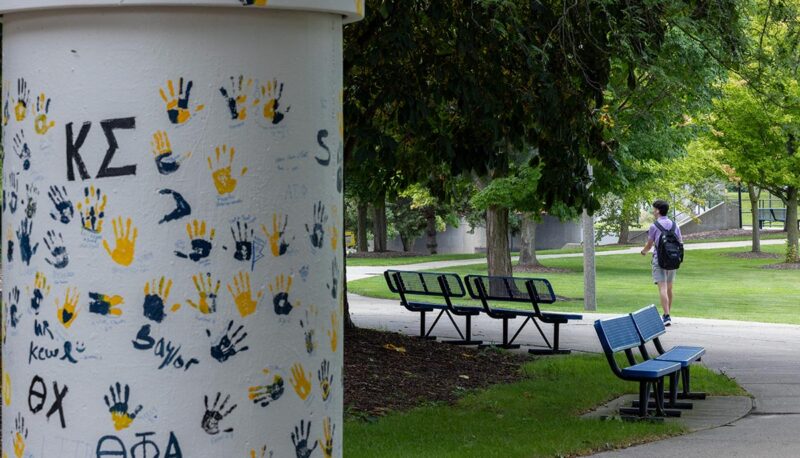 A painted pillar on campus with a student walking away in the background.