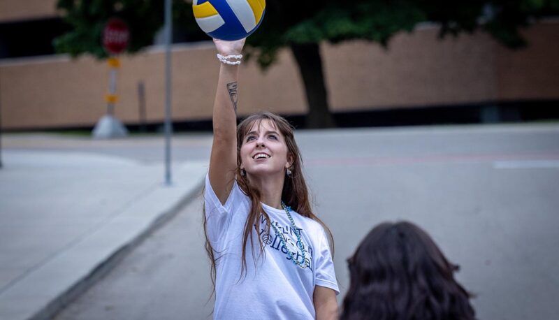 A student playing with a volleyball outside of the Rec Center.