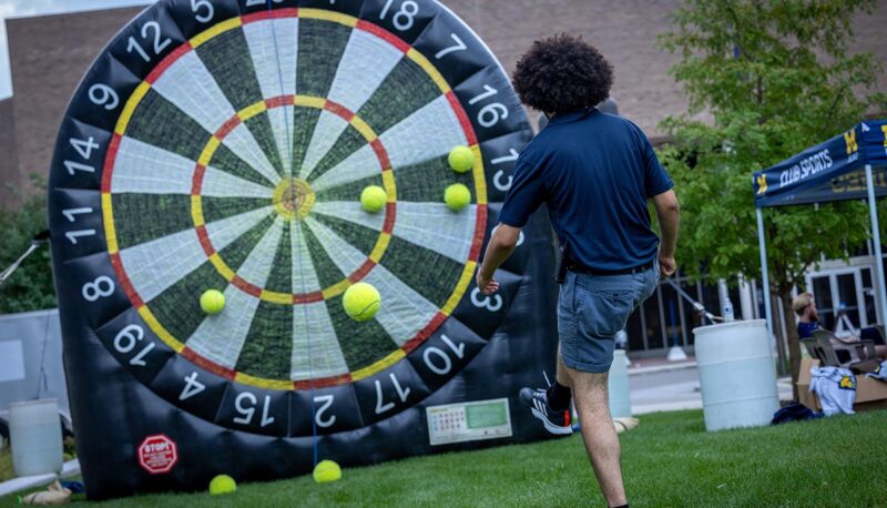 A student kicking giant tennis balls onto a giant velcro dart board.