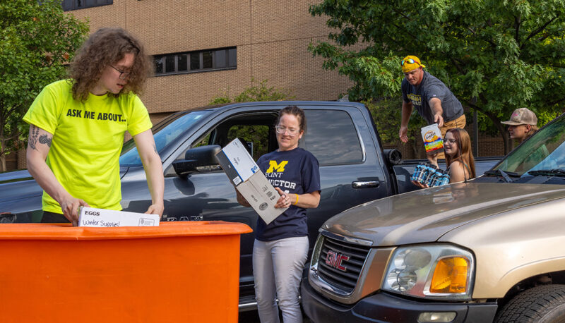 A family unloading move-in items from a truck into a bin with a volunteer helping.