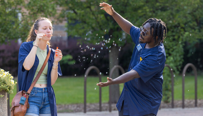 UM-Flint staff members blowing bubbles in front of First Street.