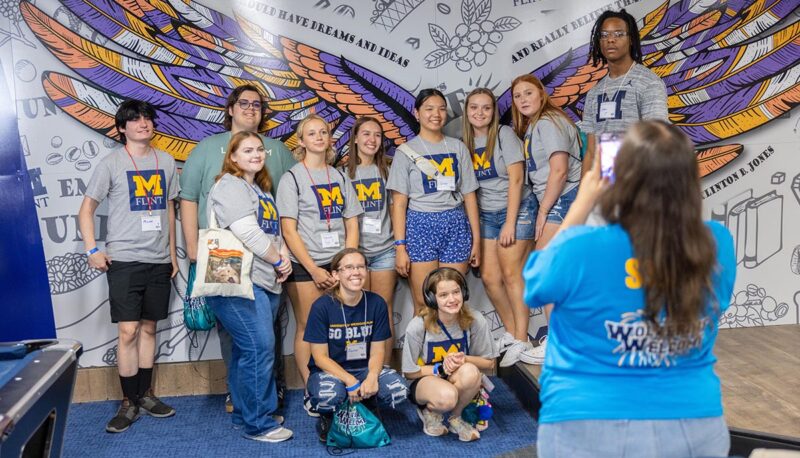 A group of students getting their picture taken in front of the mural in Clint's Cafe.