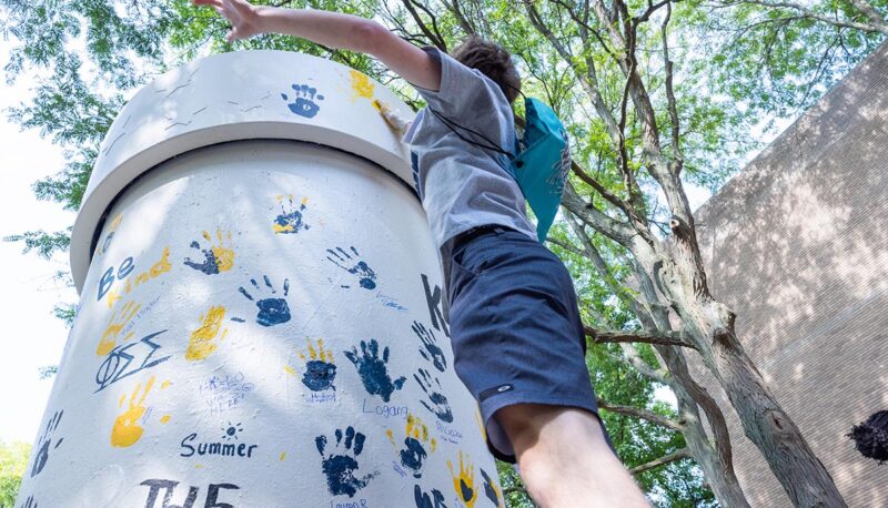 A shot from the ground up of a student jumping to put their hand print high on the pillar.