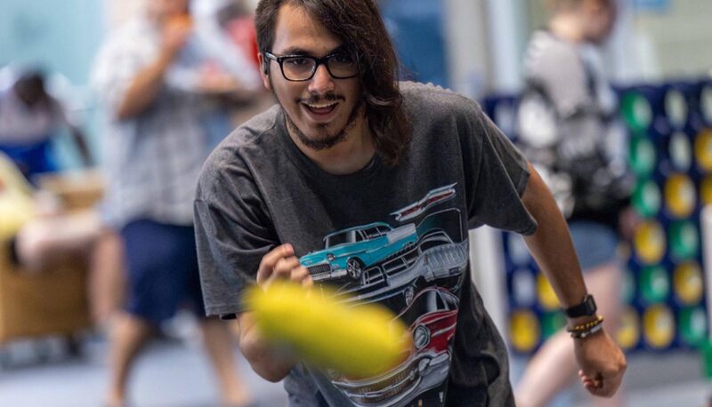 A student throwing a cornhole bag. The bag is visible mid-air.