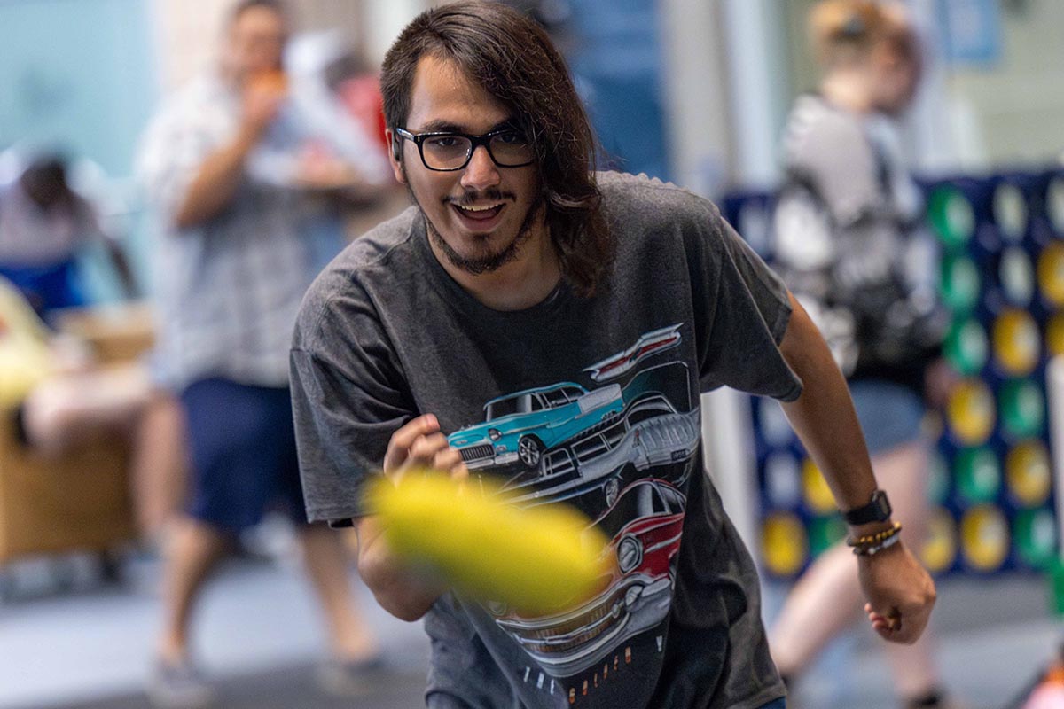 A student throwing a cornhole bag. The bag is visible mid-air.