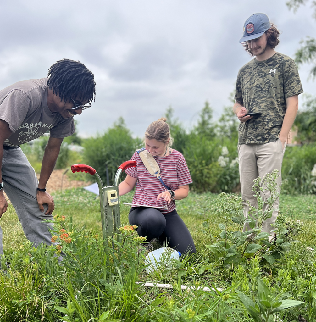 Brian Lovejoy, Northwestern University Ph.D. candidate (left), Menzies (center), and Tyler Peters (right) measure water infiltration rates in the experimental plots at the Chicago Botanic Garden. After saturating the soil, the infiltrometer is pushed into the ground and filled with water. Menzies then records how long it takes the water to absorb into the soil in each experimental plot as part of her graduate research.