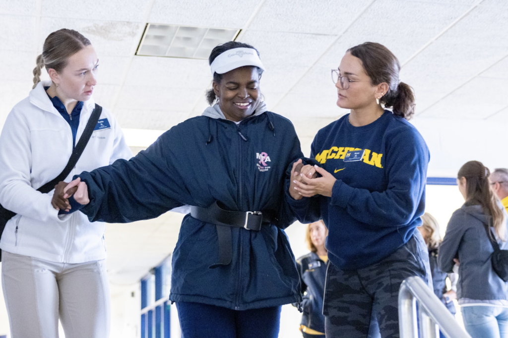 Two UM-Flint students helping a client at the HEART clinic walk down some stairs. 