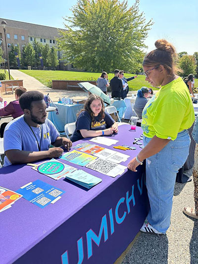 Two UM-Flint students offering voting resources to another student during an annual student orientation event