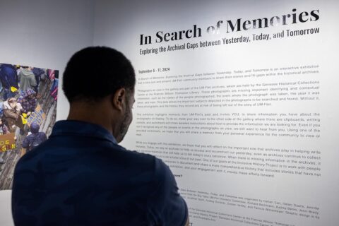 A photo from behind of a man standing and reading text on a gallery wall about "In Search of Memories."