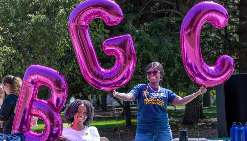 Two students holding up purple balloons that spell the letters BGC.