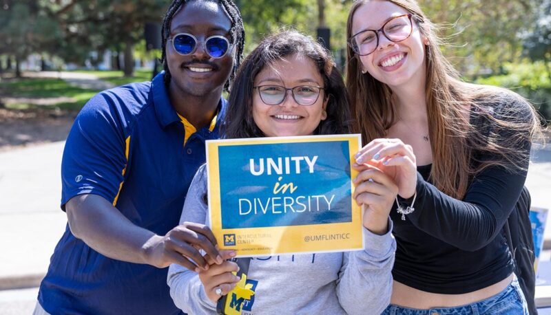 Three students holding up a sign that says unity.