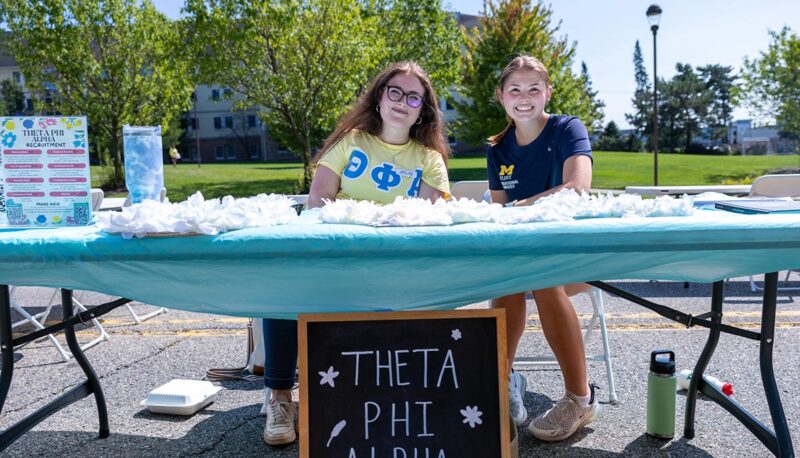 Students sitting at the Theta Phi Alpha sorority table.