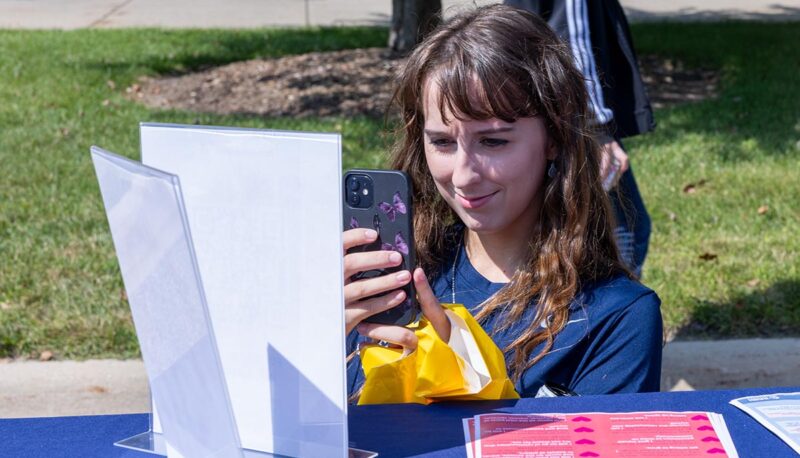 A student taking a picture with their phone of a flier at a table.