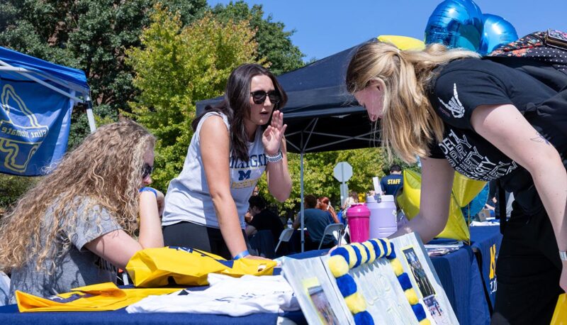 A student talking to other students at a table.