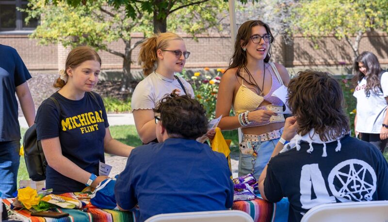 A group of students talking to other students at a table.