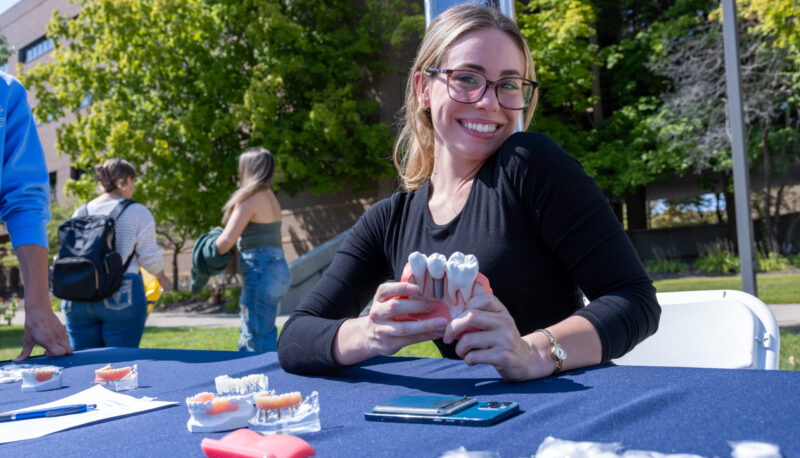 A student smiling for the camera while sitting at a table with models of the human mouth and teeth.