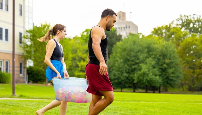 Two students carrying a bucket of water balloons.