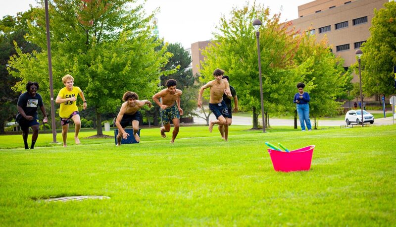 A group of students running for a bucket of water balloons on the North Lawn