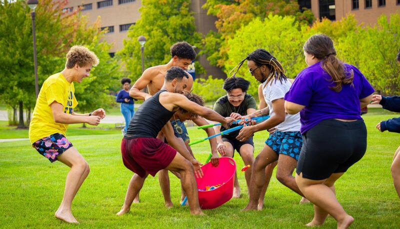 A group of students running for a bucket of water balloons on the North Lawn