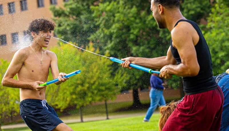 Two students squirting each other with water guns on the North Lawn.