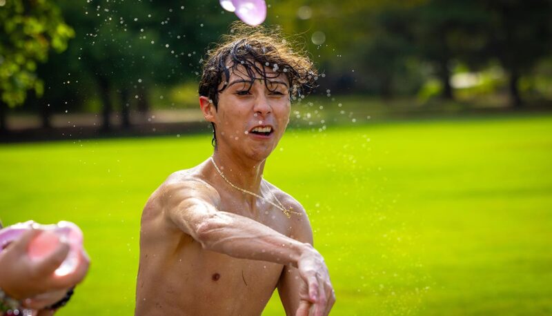 A student throwing a water balloon. The balloon's flight is captured in the photograph.