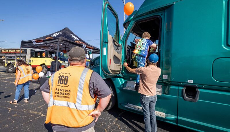 A dad helping his young child into the cab of a semi truck