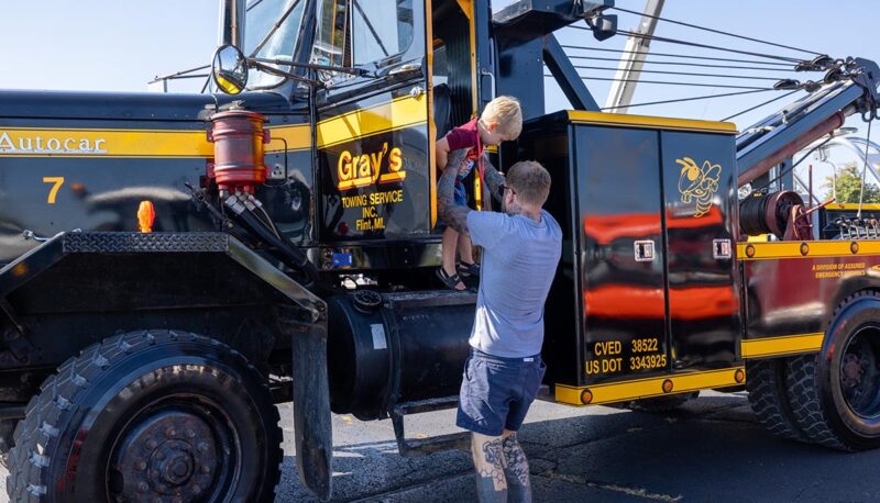 A dad helping his young child down from the driver's seat of a tow truck.