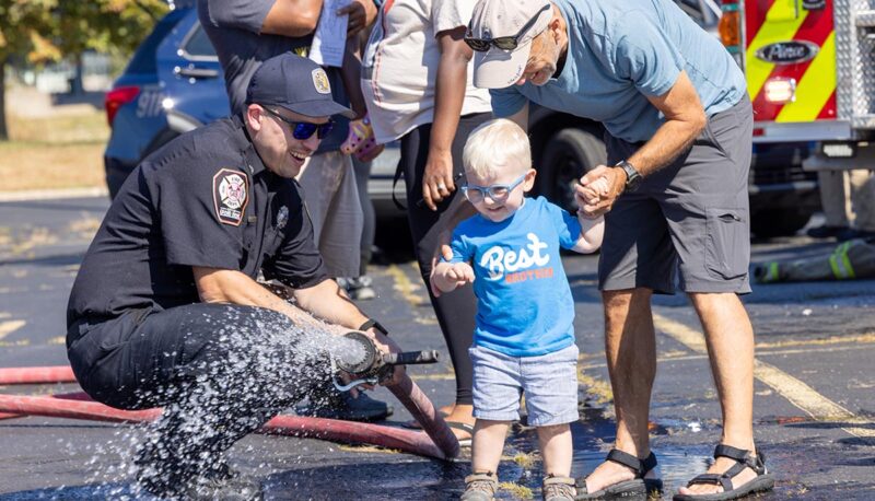 A young child seeing a firefighter play with a water hose.