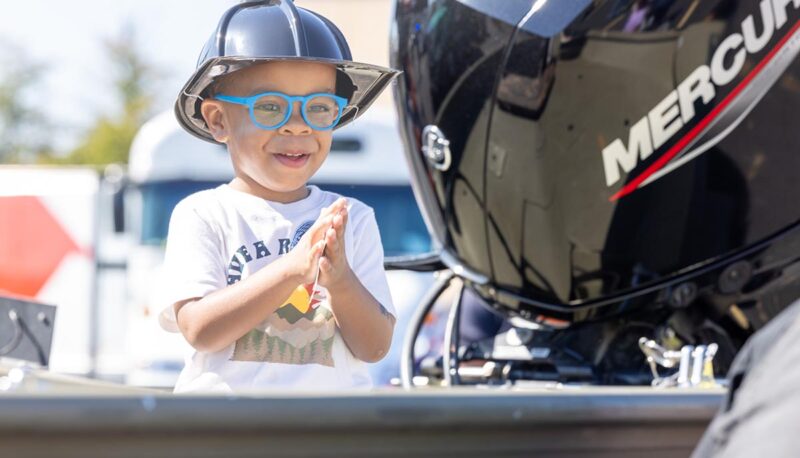 A young child wearing a firefighter helmet in a boat