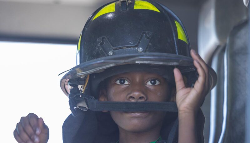 A young child putting on a firefighter helmet